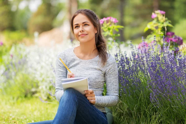 Young woman writing to notebook at summer garden — Stock Photo, Image