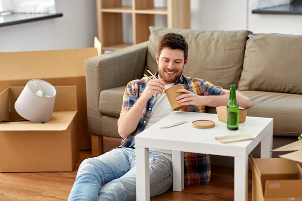 Lächelnder Mann isst im neuen Zuhause Essen zum Mitnehmen — Stockfoto