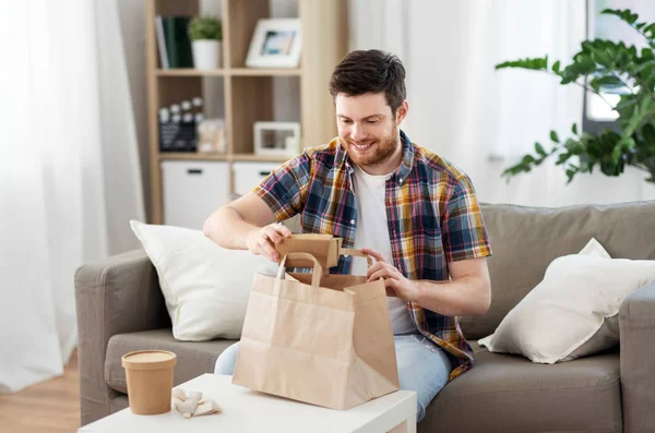 Hombre sonriente desempacando comida para llevar en casa — Foto de Stock