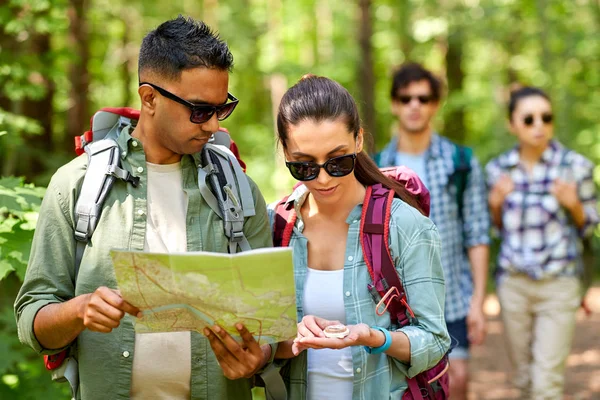 Vänner med karta och ryggsäckar vandring i skogen — Stockfoto