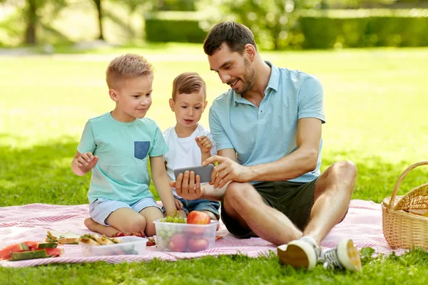 Familia con smartphone haciendo picnic en el parque —  Fotos de Stock