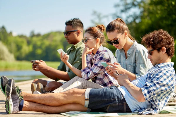 Friends with smartphone on lake pier in summer — Stock Photo, Image