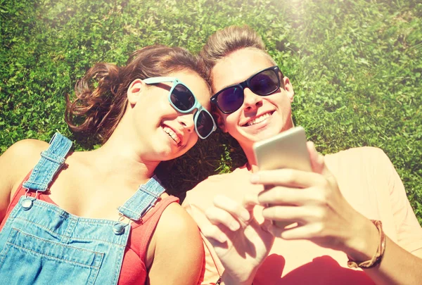 Lyckliga teenage paret smartphone liggande på gräset — Stockfoto