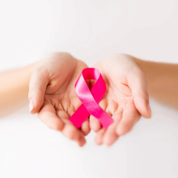 Mains féminines tenant un ruban rose de sensibilisation au cancer — Photo