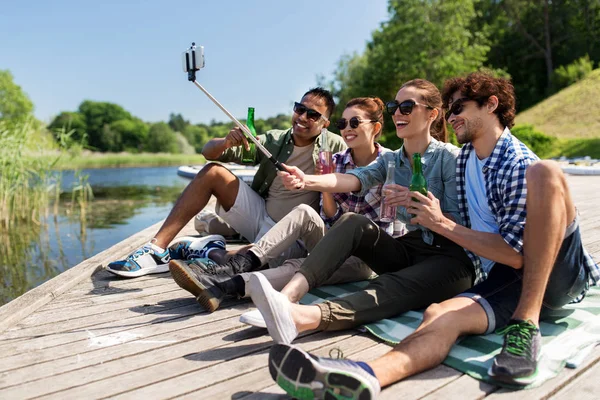 Amici con bevande prendendo selfie sul molo del lago — Foto Stock