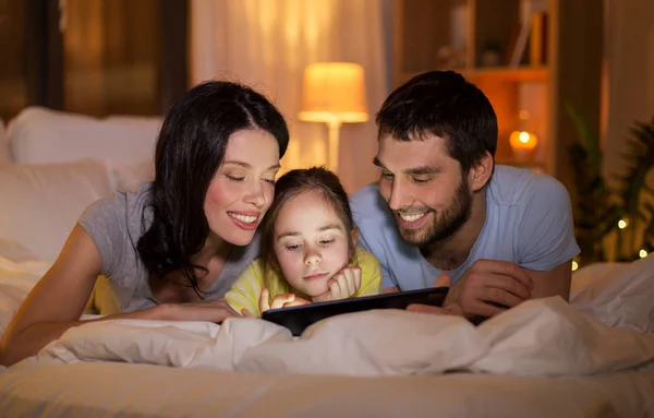Семья с планшетным компьютером в постели на ночь дома — стоковое фото