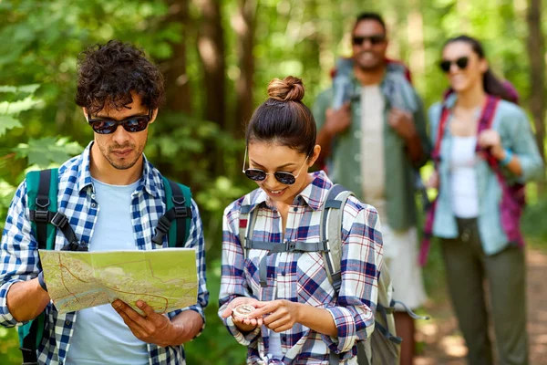 Przyjaciół z mapą i plecakami spacerujących po lesie — Zdjęcie stockowe