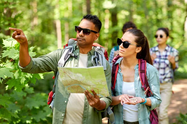 Přátelé s mapou a batohy turistika v lese — Stock fotografie