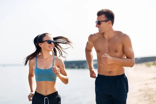 Casal em roupas esportivas correndo ao longo da praia — Fotografia de Stock