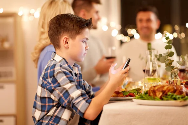 Chłopiec ze smartfonem na rodzinnej kolacji — Zdjęcie stockowe