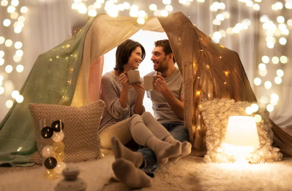 Couple drinking coffee or tea in kids tent at home — Stock Photo, Image