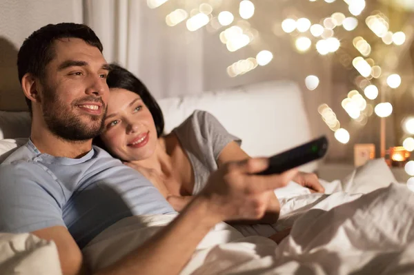 Casal feliz assistindo tv na cama à noite em casa — Fotografia de Stock