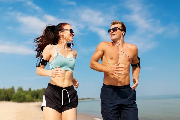 Par med telefoner och armband som löper på stranden — Stockfoto