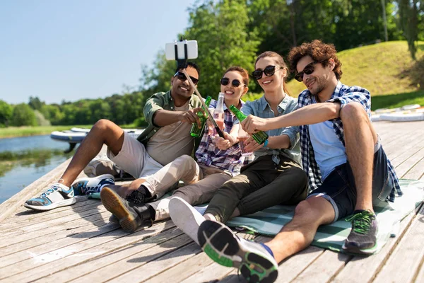 Amigos com bebidas tomando selfie no cais do lago — Fotografia de Stock