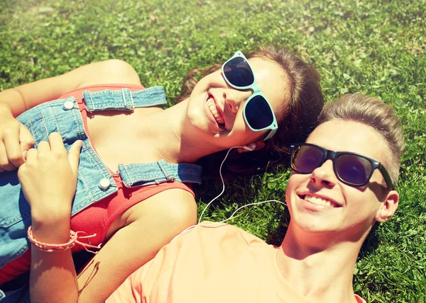 Lyckliga teenage paret med hörlurar liggande på gräset — Stockfoto