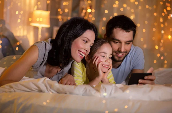 Famiglia felice con smartphone a letto di notte — Foto Stock