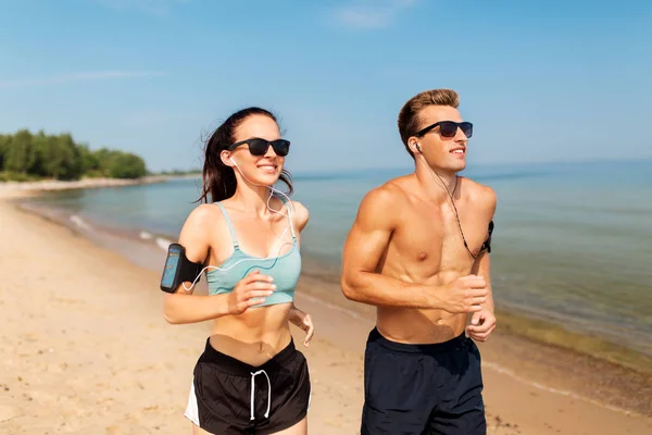 Pareja con teléfonos y brazaletes corriendo en la playa —  Fotos de Stock