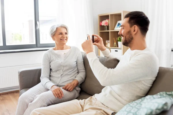 Hijo adulto fotografiando a la madre mayor en casa —  Fotos de Stock