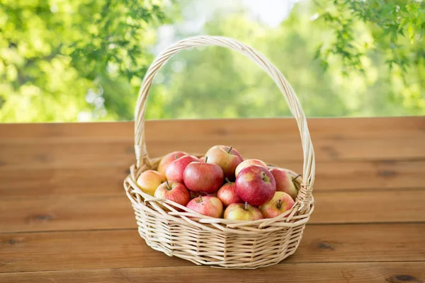 Ripe apples in wicker basket on wooden table — Stock Photo, Image