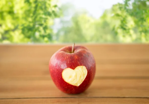Красное яблоко с вырезанным сердцем на деревянном столе — стоковое фото