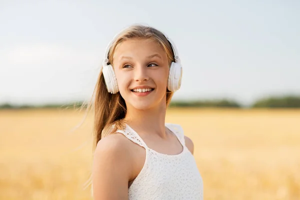 Glückliches Mädchen mit Kopfhörern auf einem Getreidefeld im Sommer — Stockfoto