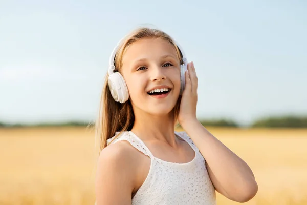 Glückliches Mädchen mit Kopfhörern auf einem Getreidefeld im Sommer — Stockfoto