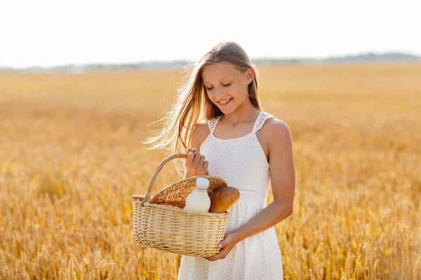 Niña con pan y leche en cesta en el campo de cereales — Foto de Stock