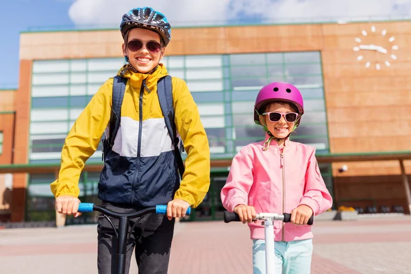 Šťastné školní děti v helmách jezdecké skútry — Stock fotografie