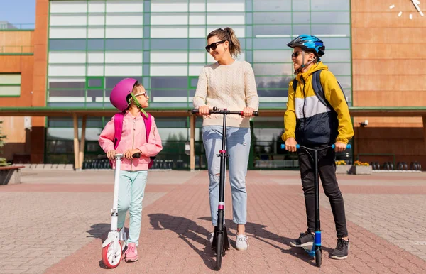 Gelukkig schoolkinderen met moeder paardrijden scooters — Stockfoto