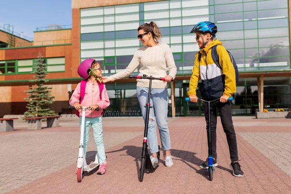 Gelukkig schoolkinderen met moeder paardrijden scooters — Stockfoto