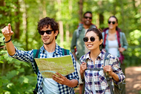 Vänner med karta och ryggsäckar vandring i skogen — Stockfoto