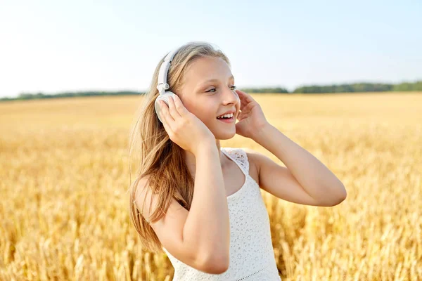 Chica feliz en auriculares en el campo de cereales en verano —  Fotos de Stock