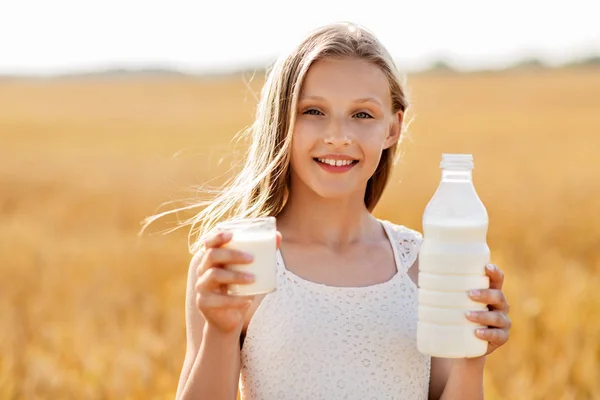 Dívka s lahví a sklenicí mléka na obilné pole — Stock fotografie