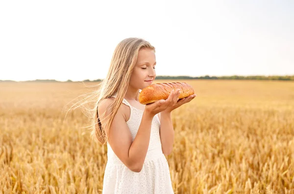 Niña oliendo pan blanco en el campo de cereales — Foto de Stock