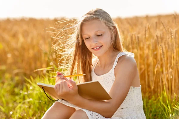 Smiling girl writing to diary on cereal field — Stock Photo, Image