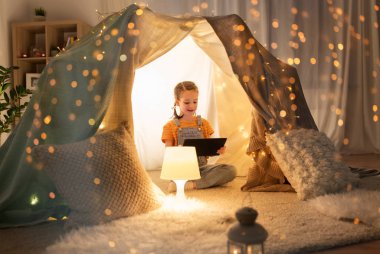 little girl with tablet pc in kids tent at home clipart