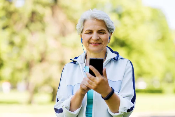 Mulher sênior desportivo com fones de ouvido e smartphone — Fotografia de Stock