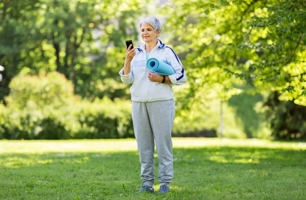 Anciana con colchoneta y smartphone en el parque —  Fotos de Stock