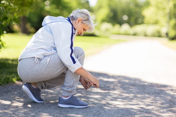 Mujer mayor atando cordones de zapatos deportivos en el parque de verano —  Fotos de Stock