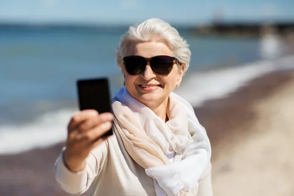 Senior vrouw neemt selfie met smartphone op het strand — Stockfoto