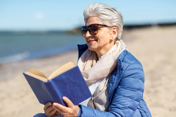 Happy senior woman reading book on summer beach — Stock Photo, Image