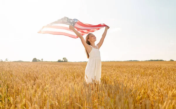 Chica con bandera americana ondeando sobre campo de cereales — Foto de Stock