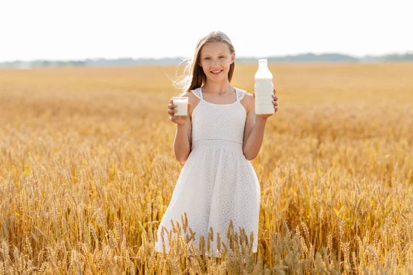 Ragazza con bottiglia e bicchiere di latte sul campo di cereali — Foto Stock