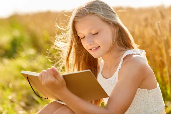 Sorrindo menina escrevendo para diário no campo de cereais — Fotografia de Stock