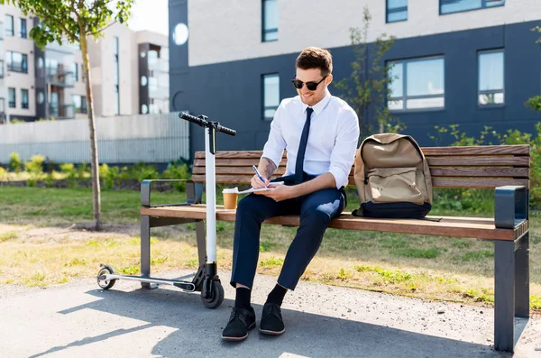 Smiling businessman writing to notebook in city — Stock Photo, Image