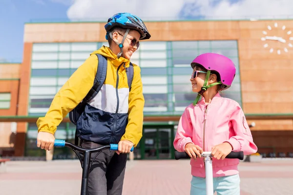 Šťastné školní děti v helmách jezdecké skútry — Stock fotografie