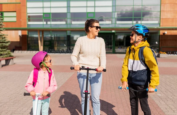 Gelukkig schoolkinderen met moeder paardrijden scooters — Stockfoto