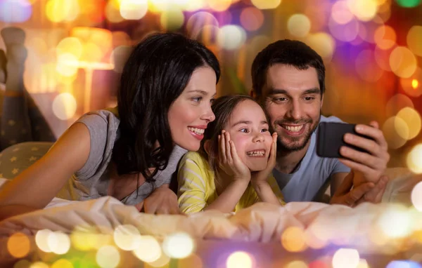 Famiglia felice con smartphone a letto di notte — Foto Stock