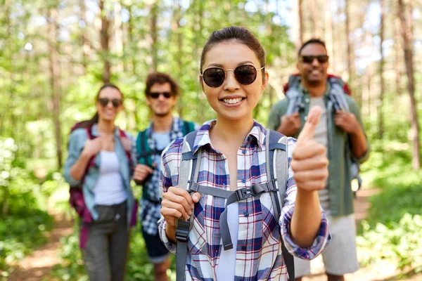 Friends with backpacks showing thumbs up in forest — Stock Photo, Image