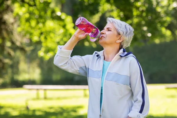 Mujer mayor bebe agua después de hacer ejercicio en el parque —  Fotos de Stock